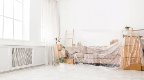 Covered sofa and stacked boxes inside a bright living room during a home renovation project. 